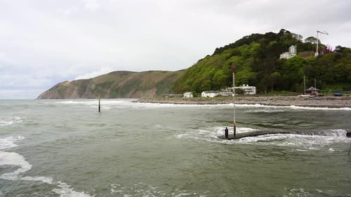 Waves roll across the sea defences of Lynmouth Harbour on a windy day. Devon coast, England, UK