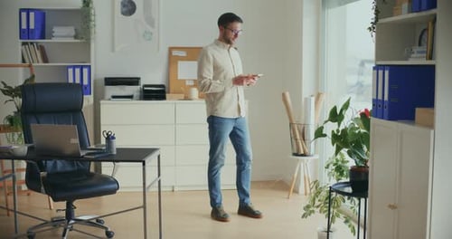 Businessman Using Smart Phone Near Window at Office