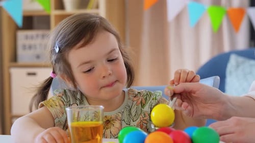 Holidays, Family And People Concept - Mother And Happy Little Baby Daughter Dyeing Easter Eggs Wi...
