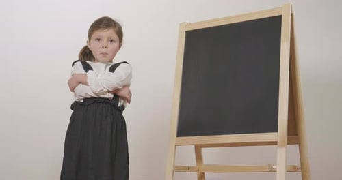 Smiling Young Girl Stands Beside a Blank Blackboard