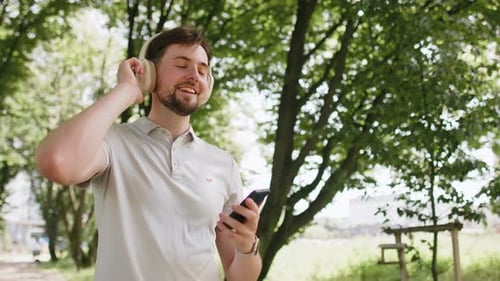 Man Listens to Music on Phone While Walking in Park