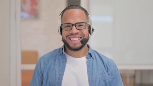 Lächelnder Afrikaner mit Headset blickt im Call Center in die Kamera