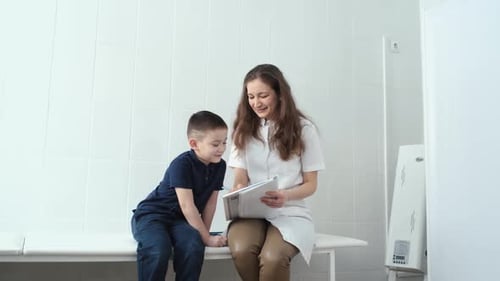 pediatrician makes notes in a notebook while sitting with a boy on a hospital couch