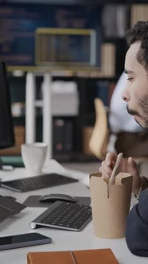 Programmierer aus dem Nahen Osten isst Mittagessen zum Mitnehmen und arbeitet im Büro am Laptop