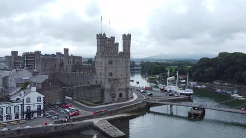 Ancient Caernarfon castle Welsh harbour town aerial view medieval waterfront landmark fast dolly lef