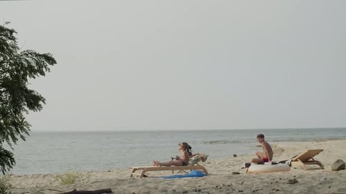 Two Boys Relaxing on the Beach on Chaise Lounges in Summer Sun