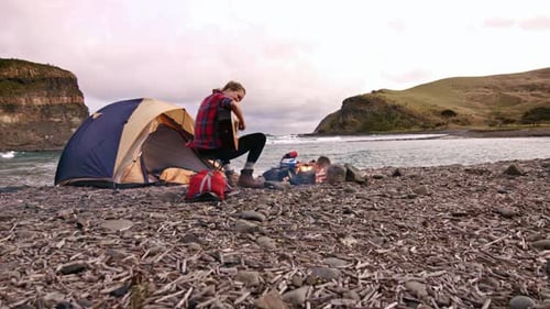 Woman plays guitar camping on rocky beach coast
