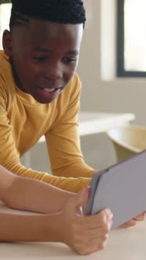 Vertical video: Noticing peer showing tablet, boy in mustard-yellow shirt leaning at table, smiling