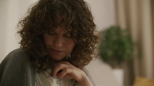 Woman Coughing Looks at Thermometer in Indoor Setting