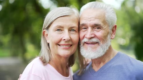 Close up portrait of married old senior couple hugging standing in city park looking at camera.