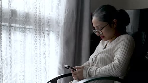Woman Using Smartphone While Sitting Near Window