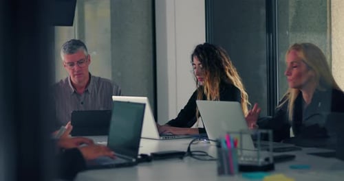 Diverse coworkers concentrate on laptops during office meeting in modern conference room,