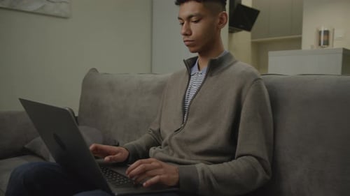 Young Adult Typing on Laptop on Gray Couch