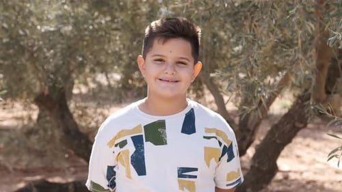 Young Boy Smiling at the Camera in the Middle of a Field
