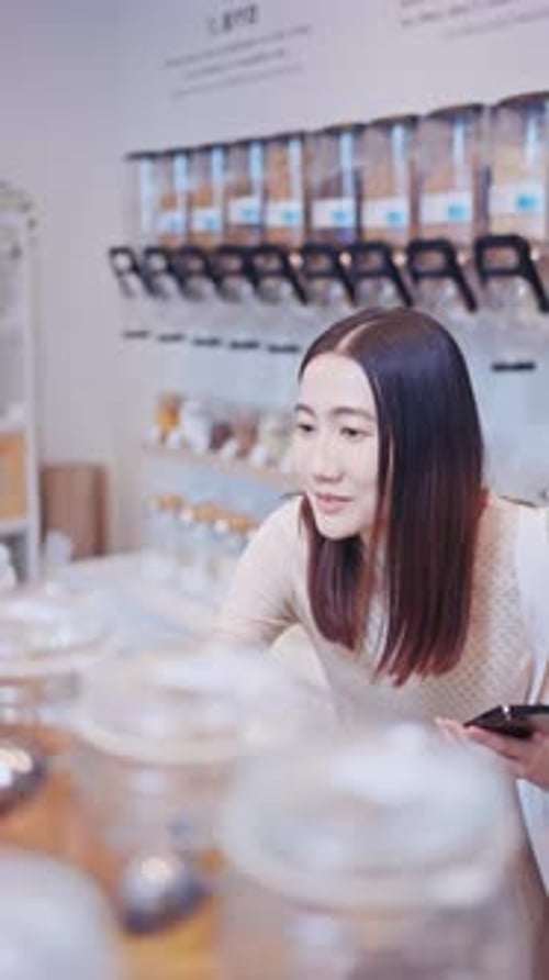 Young woman using a smartphone while shopping in a zero waste store