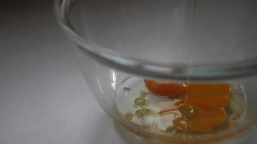 Slow motion of person pouring oil into large glass bowl with egg and yolk to bake banana bread.