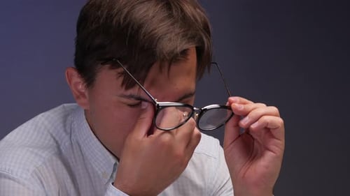 Man Removes Glasses and Rubs Tired Eyes