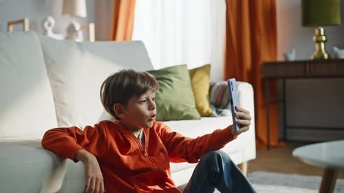 Boy in Orange Hoodie Talking on Phone at Home