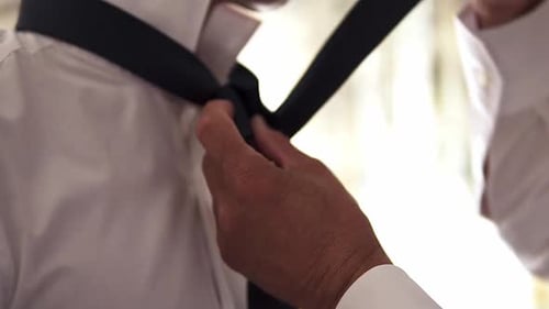 Slow motion handheld close up shot of a groom getting his tie tied by another person before his wedd