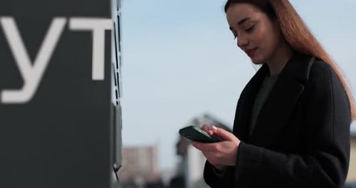 Woman Receiving Parcel From Post Terminal Machine Using Smartphone Outdoors Parcel Delivery Machine