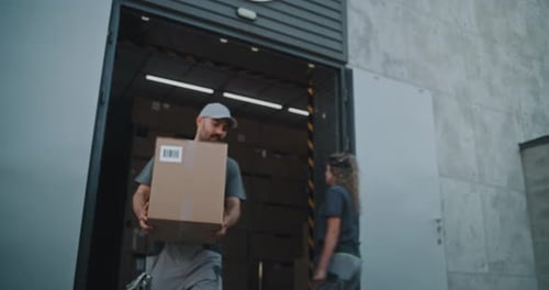 Worker Giving Cardboard Box to African American Colleague for Delivery Looking at Camera