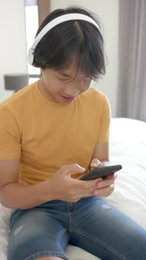 Teen Boy Using Smartphone on Bed with Headphones