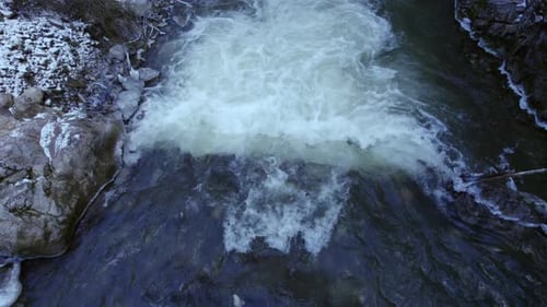 Aerial close up crossing along the mountain river with a small fall of water during the winter with
