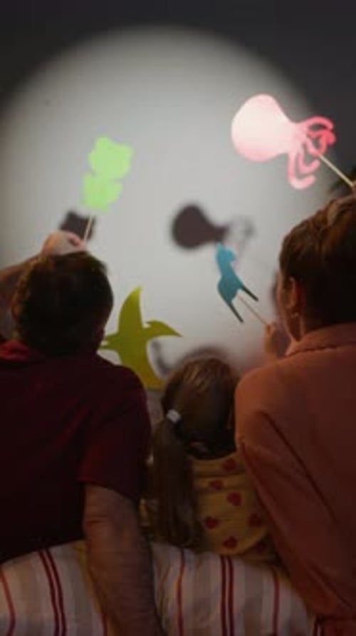 Eltern mit kleiner Tochter spielen Schattenpuppen
