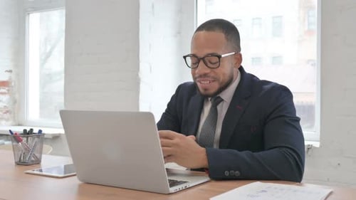 Mixed Race Businessman Chatting Online on Laptop while Sitting in Office