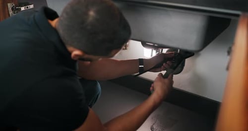 Man, plumber and wrench in kitchen for service, leak repairs and sink maintenance in apartment