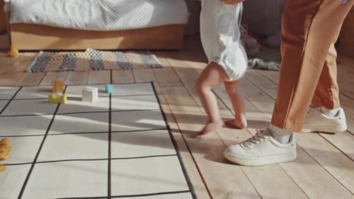 Parent Helping Toddler Learning to Walk at Home