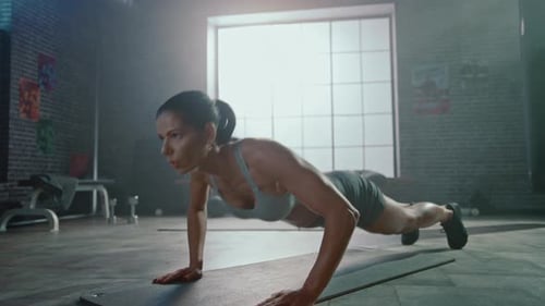 Strong and Fit Athletic Woman in Sport Top and Shorts is Doing Push Up Exercises in a Loft Style In