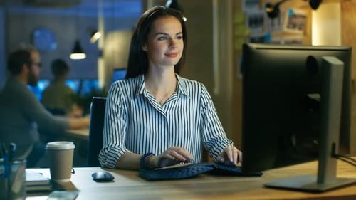 Belle jeune femme travaille sur un ordinateur personnel, elle sourit avec charme à la caméra. Elle travaille dans