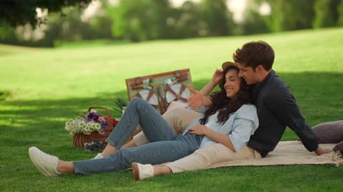 Young couple laughing together on picnic blanket at summer park in slow motion
