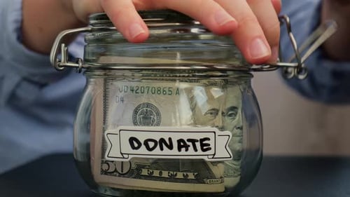 Weibliche Hände nehmen Geld vom Sparen in einem mit Dollars gefüllten Glasgefäß ab. Banknoten SPENDEN