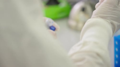 Nahaufnahme eines Wissenschaftlers in weißem Kittel und Handschuhen, der blaue flüssige Lösung im wissenschaftlichen Labor pipettiert,