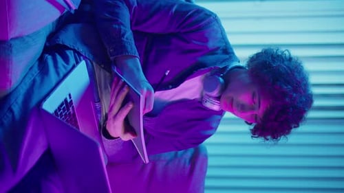 Young Adult Writing in Notebook with Laptop