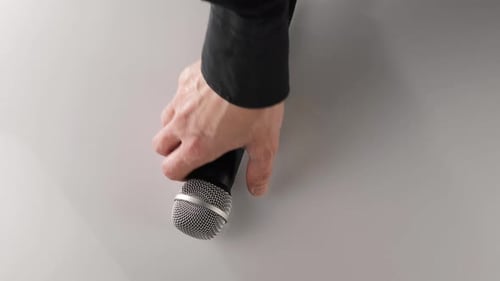 La main de l'homme prend un microphone cardioïde dans sa main sur une table blanche. Concept de séjour à la maison