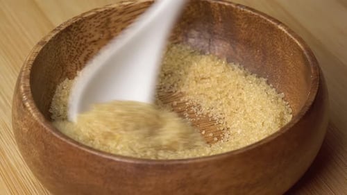 Der
Löffel nimmt Rohrzucker aus einer Holzschale auf und dreht sich auf einem Holzbrett. Brauner Zucker rotierend