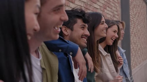 Lateral View Group of Cheerful Friends Together Leaning on Brick Wall Laughing Hugging Outdoors