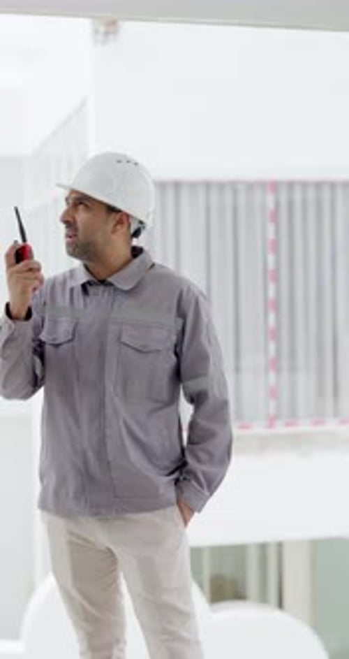 Male Engineer in Hard Hat Using Walkie-Talkie on Construction Site