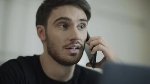 Young Man Talking on Phone Drinking Coffee Indoors