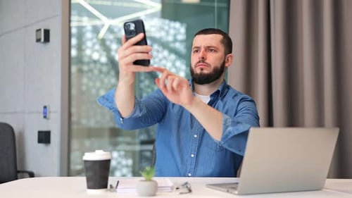 Bearded man using smartphone at office desk
