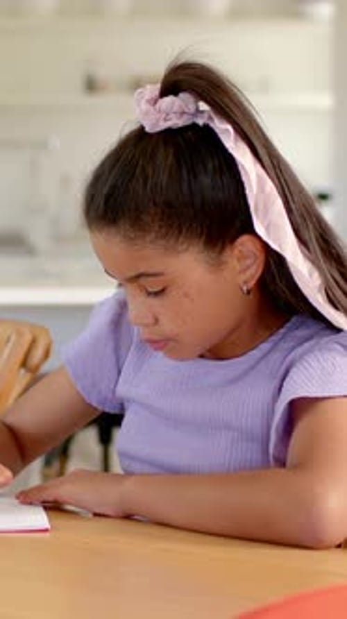 Vertical video: Writing girl doing homework, pausing and reaching for pencil at home, in lilac top