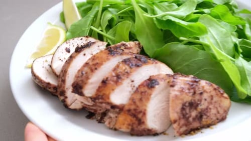 Green salad with grilled chicken breast on white plate.