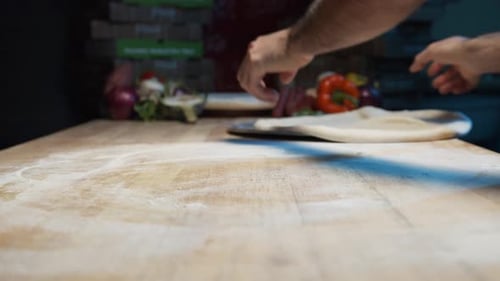 Eine Nahaufnahme der Hände eines erfahrenen Kochs legt Pizzateig auf ein Stahlblech auf eine Holztheke und lässt ihn flach werden