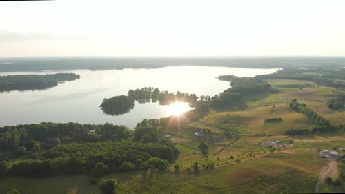 Aerial view of drone flying towards a beautiful lake over green, rural farmland countryside.