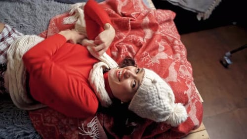 Linda dama de chapéu branco e cachecol posa deitada na cama. Vídeo sobre o espírito natalino.