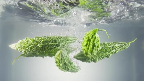 Melon amer tombant dans l'eau avec des bulles.