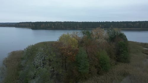 Isolated island in the middle of the lake with autumn-colored trees. Drone shot. Flying around.